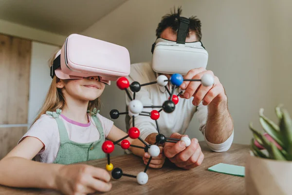 Küçük kız evde moleküler yapıyı öğrenmek için VR gözlüğü kullanarak babasıyla eğleniyor. Evde eğitim kavramı. Aile tarafından kullanılan modern teknoloji. Seçici odak.