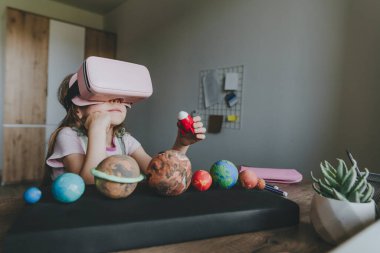 Güneş sistemi gezegenlerini öğrenmek için evde sanal gerçeklik gözlüğü kullanan küçük bir kız. Modern eğitim bilim konsepti. Seçici odak.