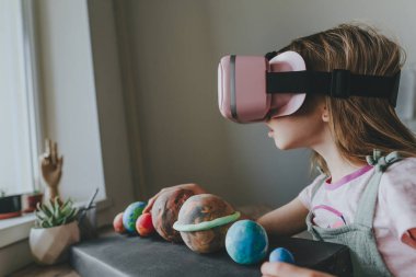 Güneş sistemi gezegenlerini öğrenmek için evde sanal gerçeklik gözlüğü kullanan küçük bir kız. Modern eğitim bilim konsepti. Seçici odak.