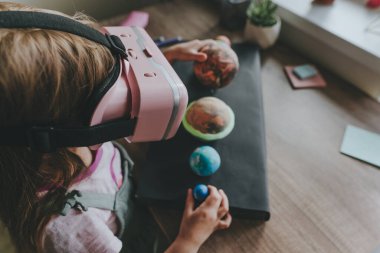 Güneş sistemi gezegenlerini öğrenmek için evde sanal gerçeklik gözlüğü kullanan küçük bir kız. Modern eğitim bilim konsepti. Seçici odak.