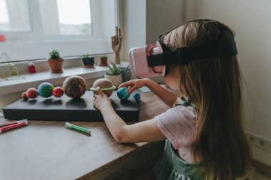 Güneş sistemi gezegenlerini öğrenmek için evde sanal gerçeklik gözlüğü kullanan küçük bir kız. Modern eğitim bilim konsepti. Seçici odak.