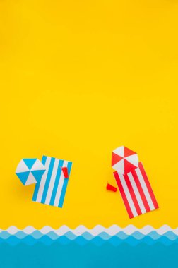 Kağıt plaj havlusu, kumsalda şemsiye, oyuncak içecek ve güneş gözlüğü. Yaz tatili minimalist yaratıcı tasarım konsepti. Metin için boş alanı olan kağıt sanatı arkaplanı.
