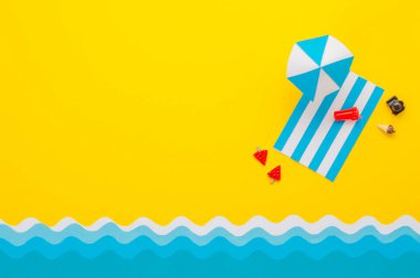 Kağıt plaj havlusu, kumsalda şemsiye, oyuncak içecek ve güneş gözlüğü. Yaz tatili minimalist yaratıcı tasarım konsepti. Metin için boş alanı olan kağıt sanatı arkaplanı.