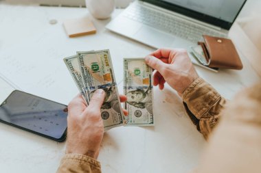 El yazısıyla hesaplama yaparak Amerikan dolarlarını sayan genç adama yaklaş. Planlama bütçesi. Seçici odak.