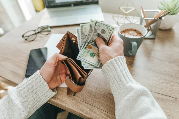 Delikanlının cüzdanından Amerikan doları çıkarmasına yakın çekim. Akıllı telefondaki hesap makinesi uygulamasını kullanarak ve el yazısıyla hesaplama yaparak bütçe planlaması. Seçici para odaklı.