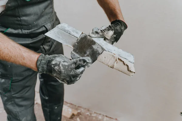 Male builder in work overalls plastering a wall using a construction trowel. Horizontal panorama banner with blank space for text.