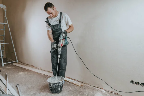 Male builder in work overalls kneading a solution using a construction perforator for plastering.