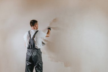 İş tulumlu erkek müteahhit inşaat malası kullanarak duvarı sıvıyor. Metin için boş alanı olan yatay panorama pankartı.