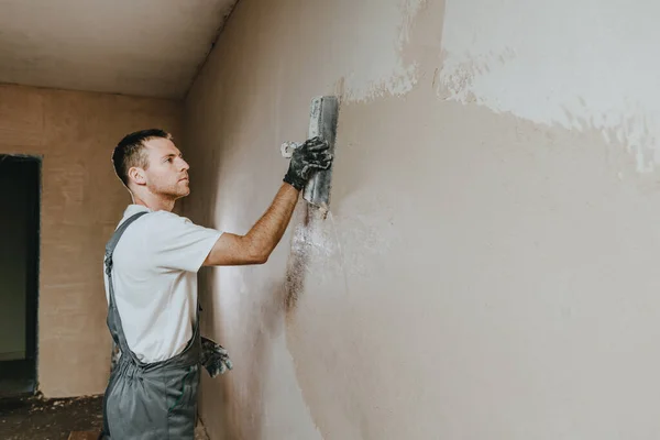 Male builder in work overalls plastering a wall using a construction trowel. Horizontal panorama banner with blank space for text.