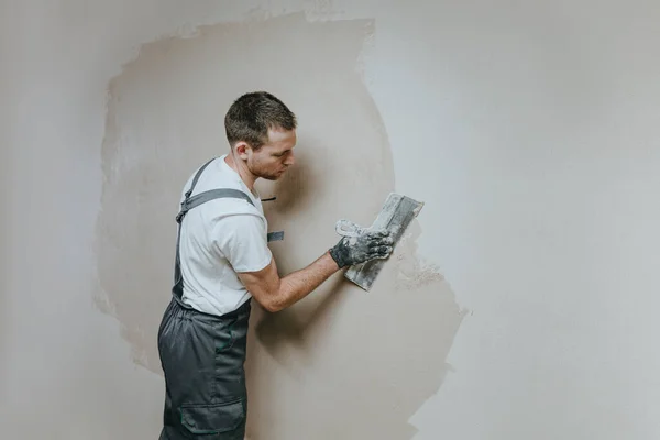 Male builder in work overalls plastering a wall using a construction trowel. Horizontal panorama banner with blank space for text.