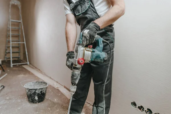 Male builder in work overalls kneading a solution using a construction perforator for plastering.