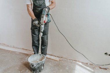İş tulumlu erkek müteahhit sıva için bir inşaat delgisini kullanarak çözeltiyi yoğuruyor..