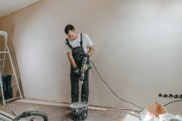 Male builder in work overalls kneading a solution using a construction perforator for plastering.