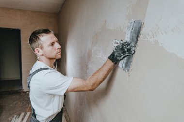 İş tulumlu erkek müteahhit inşaat malası kullanarak duvarı sıvıyor. Metin için boş alanı olan yatay panorama pankartı.