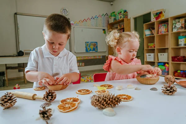 Çocuklar hamur üzerinde parmak izi yapıyorlar. Doğal malzemeler kullanıyorlar. Portakal dilimleri, koniler, kabuklar, anaokulundaki tüyler. Erken kalkınma kavramı.