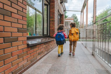 Back view of two little girls with backpacks holding hands going to an elementary school. Back to school concept. Selective focus on girls.