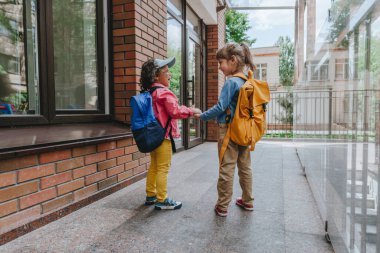 Back view of two little girls with backpacks going to an elementary school. Back to school concept. Selective focus on girls.