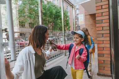 Happy smiling woman teacher greeting elementary school student at first day at school standing near the open door outside. Selective focus.