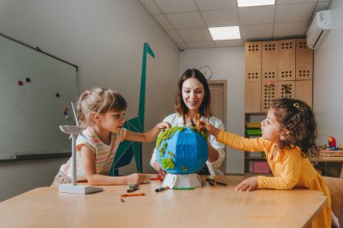 Natural science or Geography lesson at elementary school or kindergarten. Students playing with wild animals toys on handmade globe in the classroom. Selective focus.