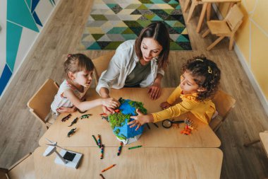 Natural science or Geography lesson at elementary school or kindergarten. Students playing with wild animals toys on handmade globe in the classroom. Selective focus.
