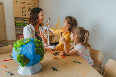 Natural science or Geography lesson at elementary school or kindergarten. Students playing with wild animals toys on handmade globe in the classroom. Selective focus.