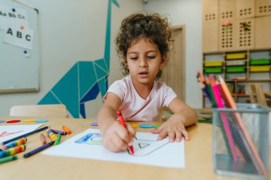 English lesson at elementary school or kindergarten. Girl learning the alphabet and colors coloring the letter A. Selective focus.