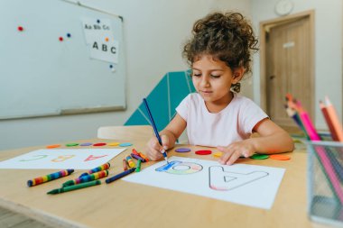 English lesson at elementary school or kindergarten. Girl learning the alphabet and colors coloring the letter A. Selective focus.
