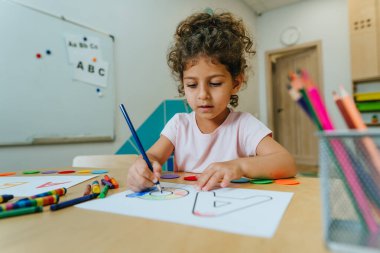 English lesson at elementary school or kindergarten. Girl learning the alphabet and colors coloring the letter A. Selective focus.