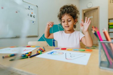 English lesson at elementary school or kindergarten. Girl learning the alphabet and colors coloring the letter A. Selective focus.