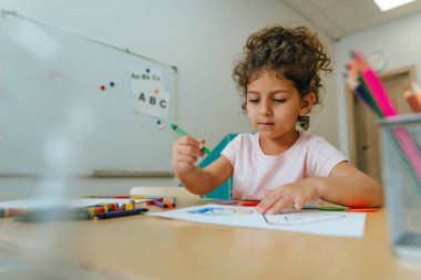 English lesson at elementary school or kindergarten. Girl learning the alphabet and colors coloring the letter A. Selective focus.