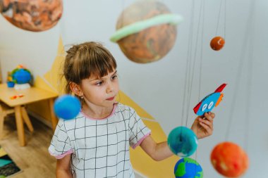 Little girl playing with paper spaceship learning Solar system planets models at home or kindergarten. Education science concept. Selective focus.