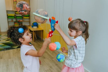 Little girl playing with paper spaceship learning Solar system planets models at home or kindergarten. Education science concept. Selective focus.