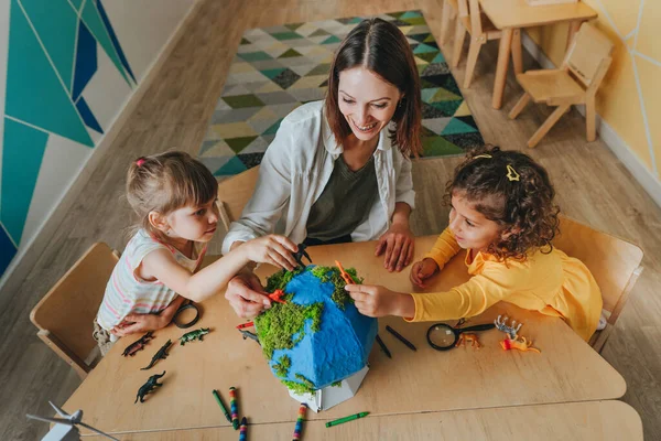 Natural science or Geography lesson at elementary school or kindergarten. Students playing with wild animals toys on handmade globe in the classroom. Selective focus.