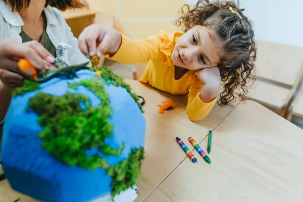 Natural science or Geography lesson at elementary school or kindergarten. Students playing with wild animals toys on handmade globe in the classroom. Selective focus.