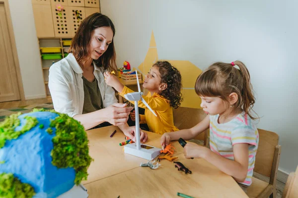 Natural science or Geography lesson at elementary school or kindergarten. Students playing with wild animals toys on handmade globe in the classroom. Selective focus.