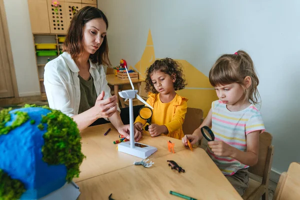 Natural science or Geography lesson at elementary school or kindergarten. Students playing with wild animals toys on handmade globe in the classroom. Selective focus.