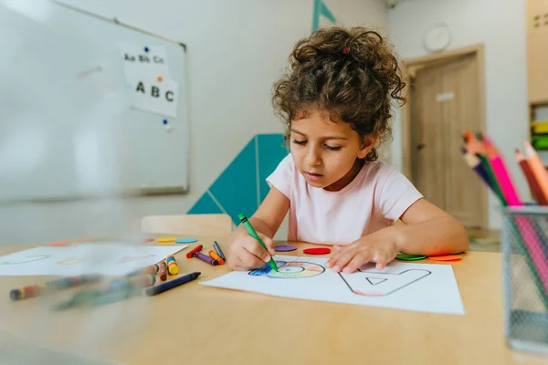 English lesson at elementary school or kindergarten. Girl learning the alphabet and colors coloring the letter A. Selective focus.