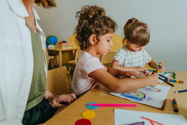 English lesson at elementary school or kindergarten. Students learning alphabet and colors with teacher coloring the letter A sitting in the classroom. Selective focus.