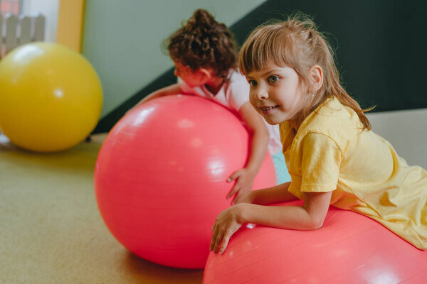 Little girls sitting near the exercise ball in sport gym. Preschoolers doing exercises on the mat. Health concept.