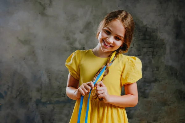 小女孩用黄色的蓝丝带在黑暗的阁楼背景下编织她的头发 上面有空白的文字空间 — 图库照片