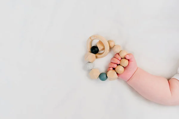 Baby's hand holding beaded teether. Wooden toys on white textile background with blank space for text. Eco friendly non plastic toys concept. Top view, flat lay.