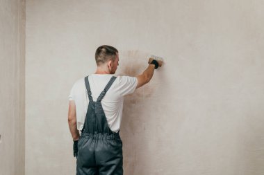 Tulumlu bir erkek işçi. Duvara boya fırçası yapıştırıyor. Seçici odak.