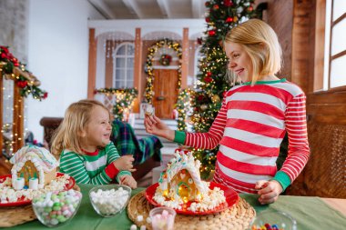 Geleneksel Noel pastalarını süsleyen çizgili pijama giyen iki kız kardeş mutfakta kremalı ve şekerli zencefilli evler. Seçici odak.