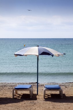 Çift şezlong ve plaj şemsiyesi ıssız bir sahilde