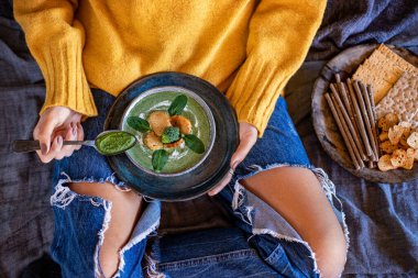 Genç bir kız çorbasını yatağında içiyor. Sebze çorbası konsepti. 