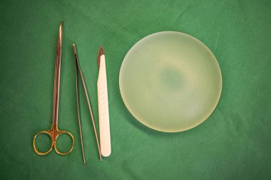 Ameliyat masasına cerrahi makas, cımbız, neşter ve silikon göğüs implantı yerleştirilir..