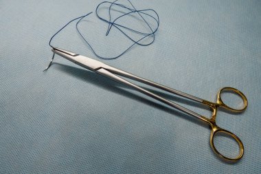 Cerrahi dikiş iğnenin sapına tutturulur ve yanında da bir çift cımbız bulunur.