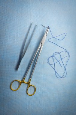 Cerrahi dikiş iğnenin sapına tutturulur ve yanında da bir çift cımbız bulunur.