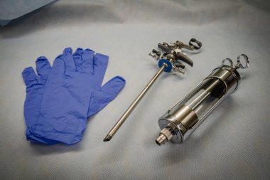 instrument for performing a prostate resection lies next to blue medical gloves and a glass bulb syringe clipart