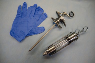 Prostat rezeksiyonu için kullanılan enstrüman mavi tıbbi eldiven ve cam şırınganın yanında yatıyor.